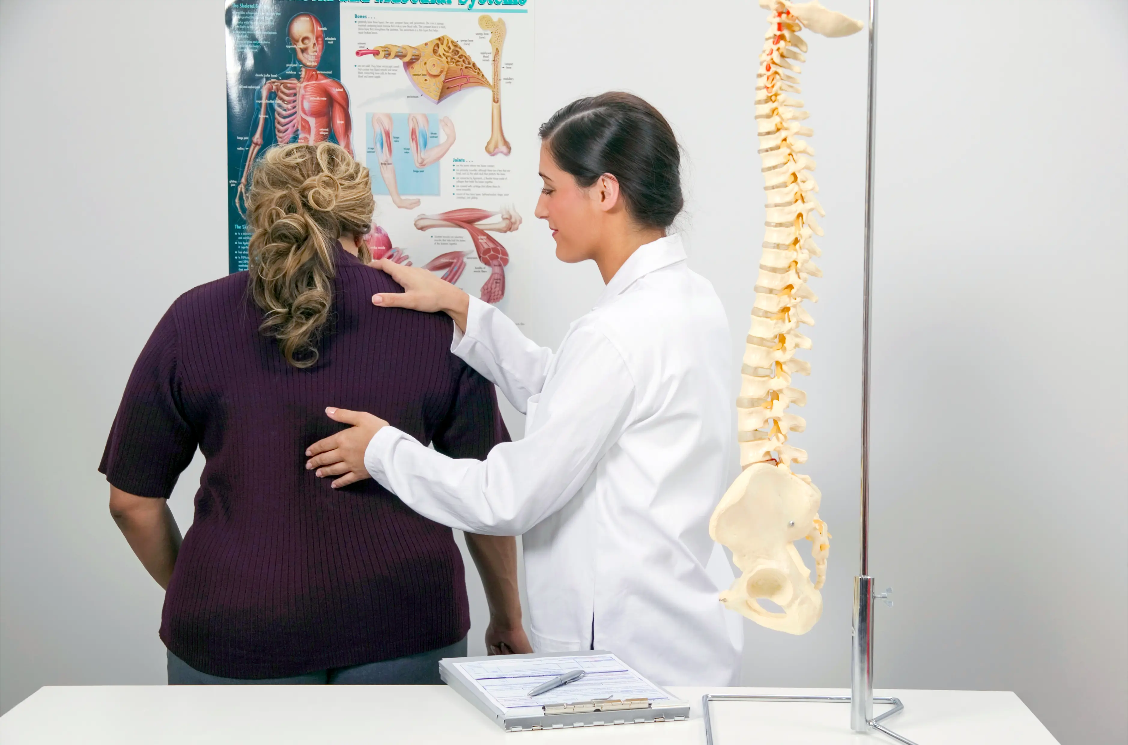 a woman getting a chiropractic consult in an office with a model of the human spine visible
